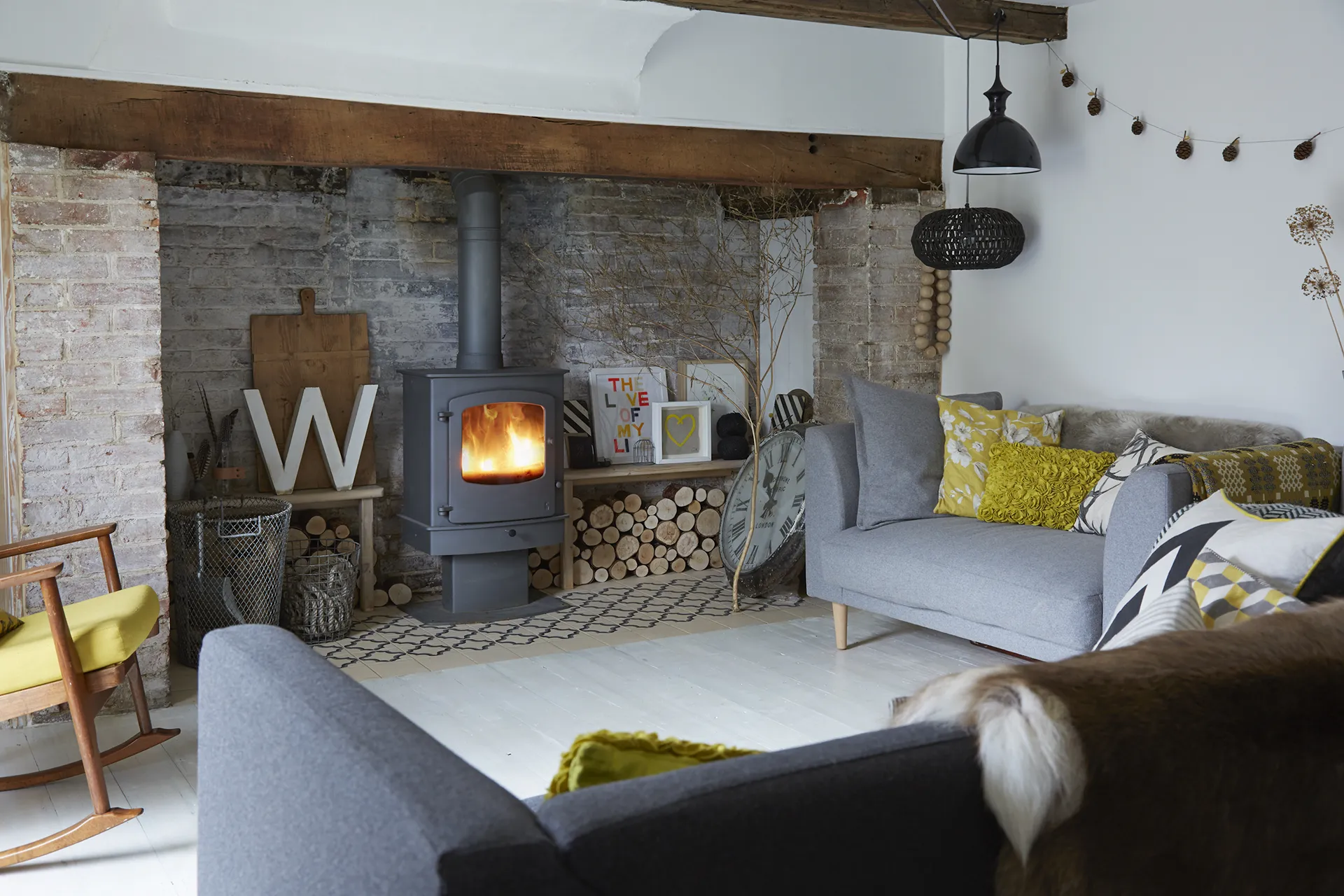 Cozy living room with a wood-burning stove, gray sofas with yellow pillows, and rustic decor.