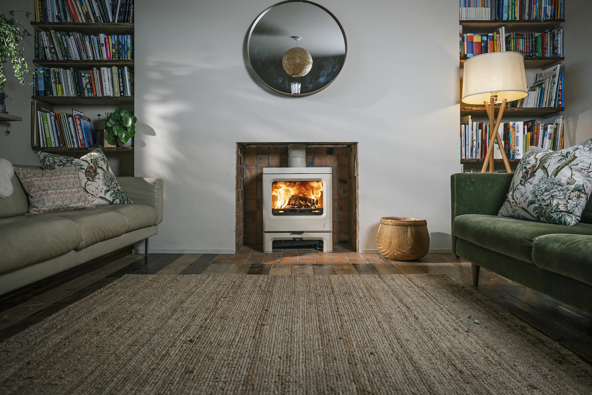 Living room with a wood-burning stove, beige and green sofas, bookshelves, and a floor lamp.