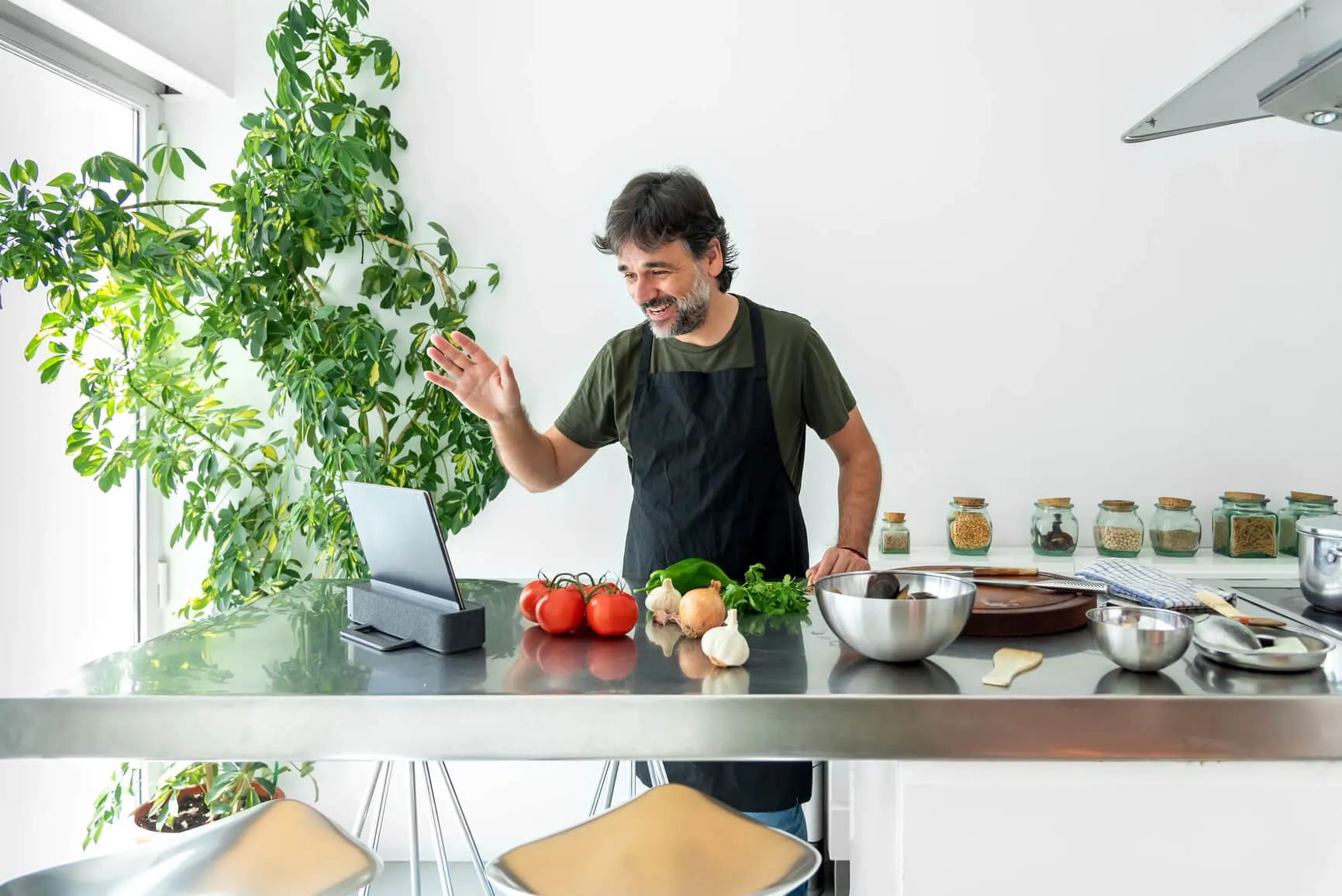 Homme dans une cuisine saluant devant un ordinateur portable entouré de légumes frais.