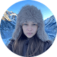 Portrait of a young woman wearing a furry hat with snowy mountain peaks in the background.