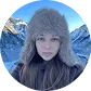 Portrait of a young woman wearing a furry hat with snowy mountain peaks in the background.