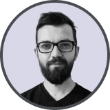 Portrait of a bearded man wearing glasses and a black shirt against a light purple background.