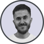 Headshot of a smiling man with short dark hair and a beard against a light gray background.