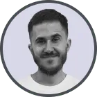 Headshot of a smiling man with short dark hair and a beard against a light gray background.