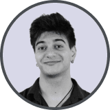 Smiling young man with dark hair and earring wearing a black shirt, on light gray background.