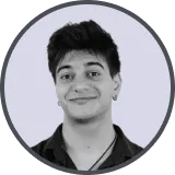 Smiling young man with dark hair and earring wearing a black shirt, on light gray background.