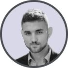 Headshot of a young man with short dark hair and a trimmed beard, wearing a collared shirt under a blazer, smiling slightly.