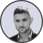 Headshot of a young man with short dark hair and a trimmed beard, wearing a collared shirt under a blazer, smiling slightly.