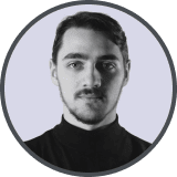 Portrait of a young woman with long dark hair and bangs wearing a black top, smiling slightly against a light purple background.