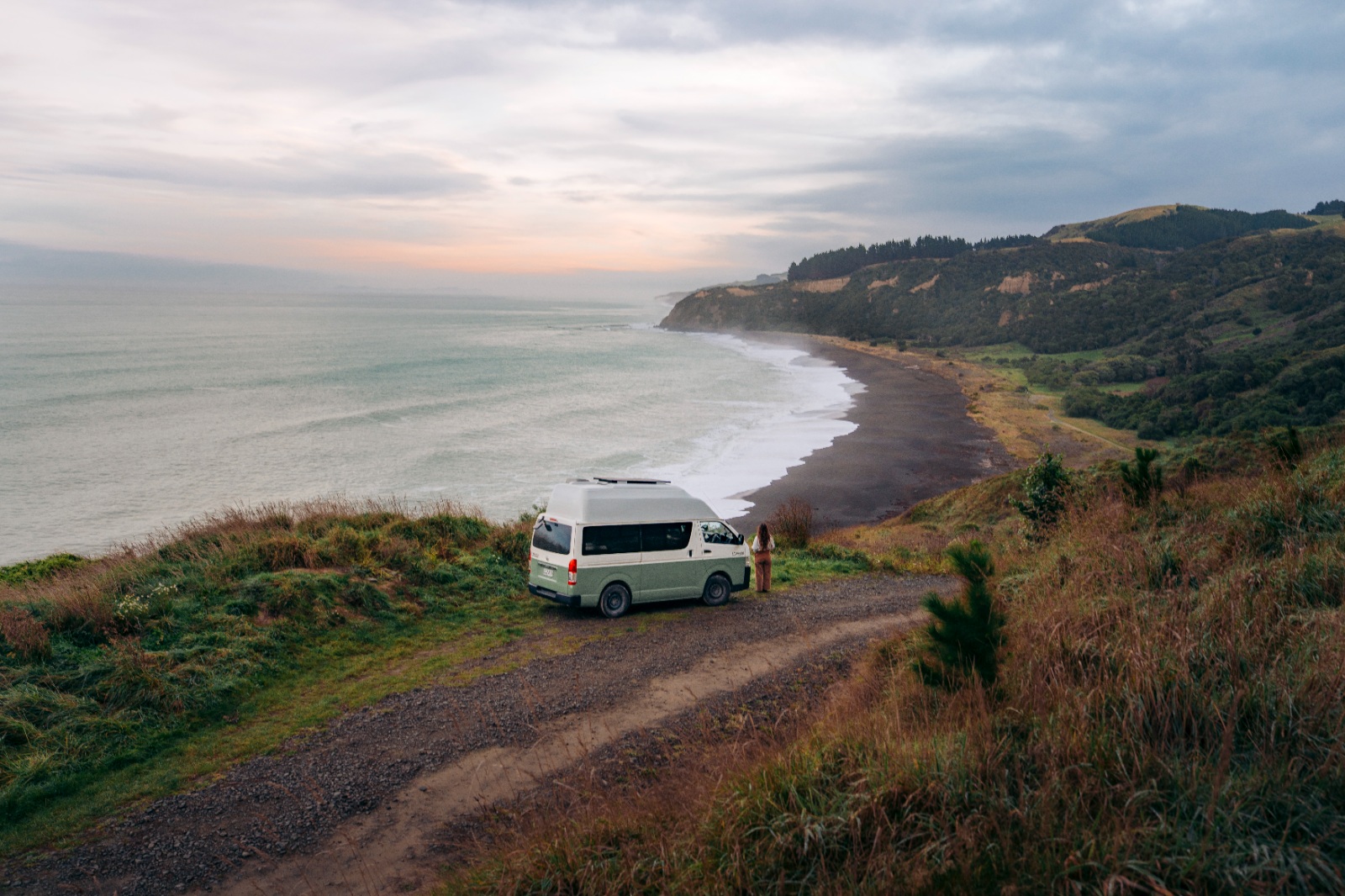 Big Little Campers high-top campervan parked on a clifftop above a long beach