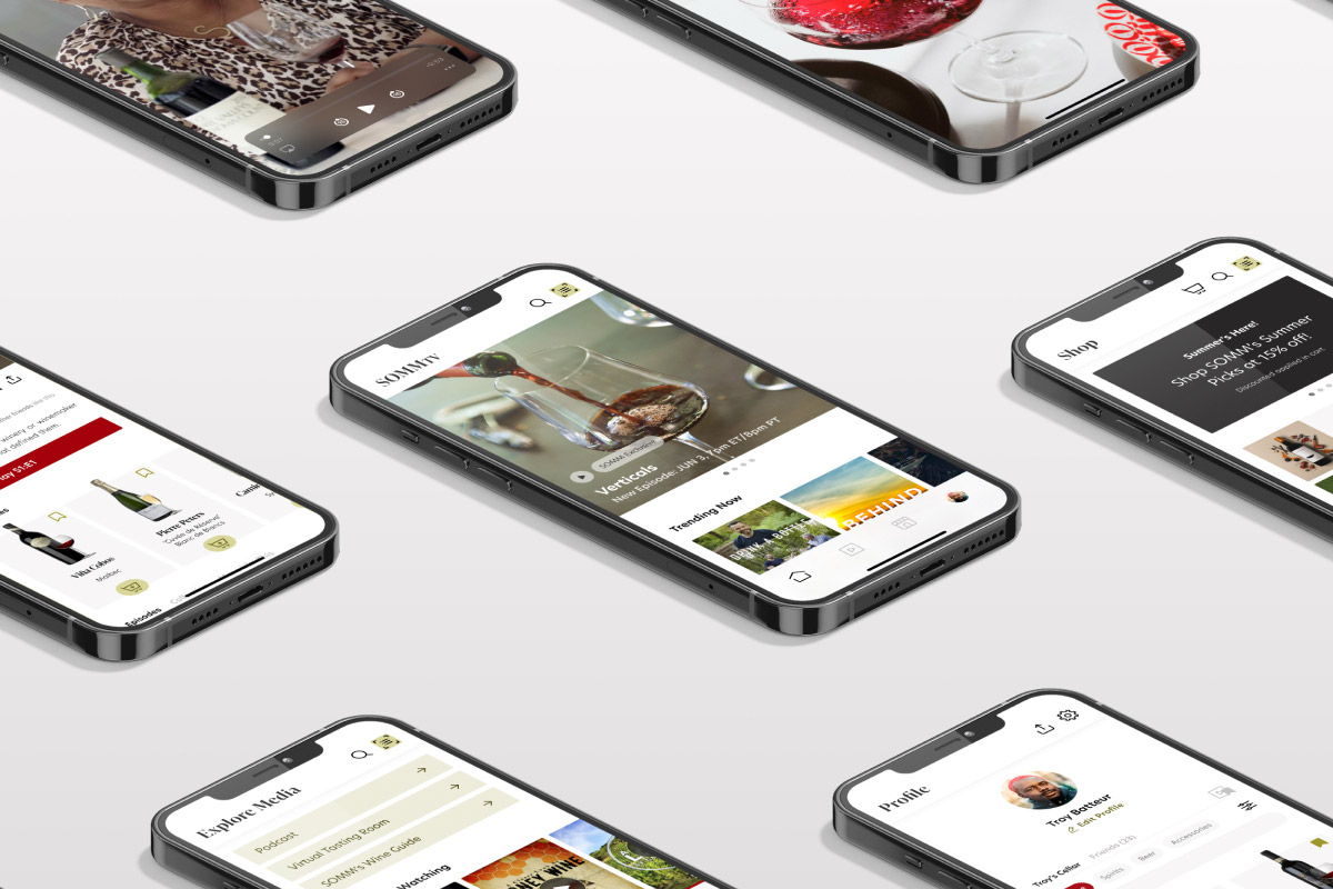 A collection of smartphone screens is arranged across a light gray background, each displaying different sections of the SOMM TV app. Visible screens feature wine-focused video content, shopping experiences, media exploration tools, user profiles, and product listings. The central screen highlights a featured wine video, while surrounding screens show educational content, wine recommendations, and community features. The clean layout and modern device mockups emphasize the app’s blend of streaming, discovery, and wine lifestyle content.