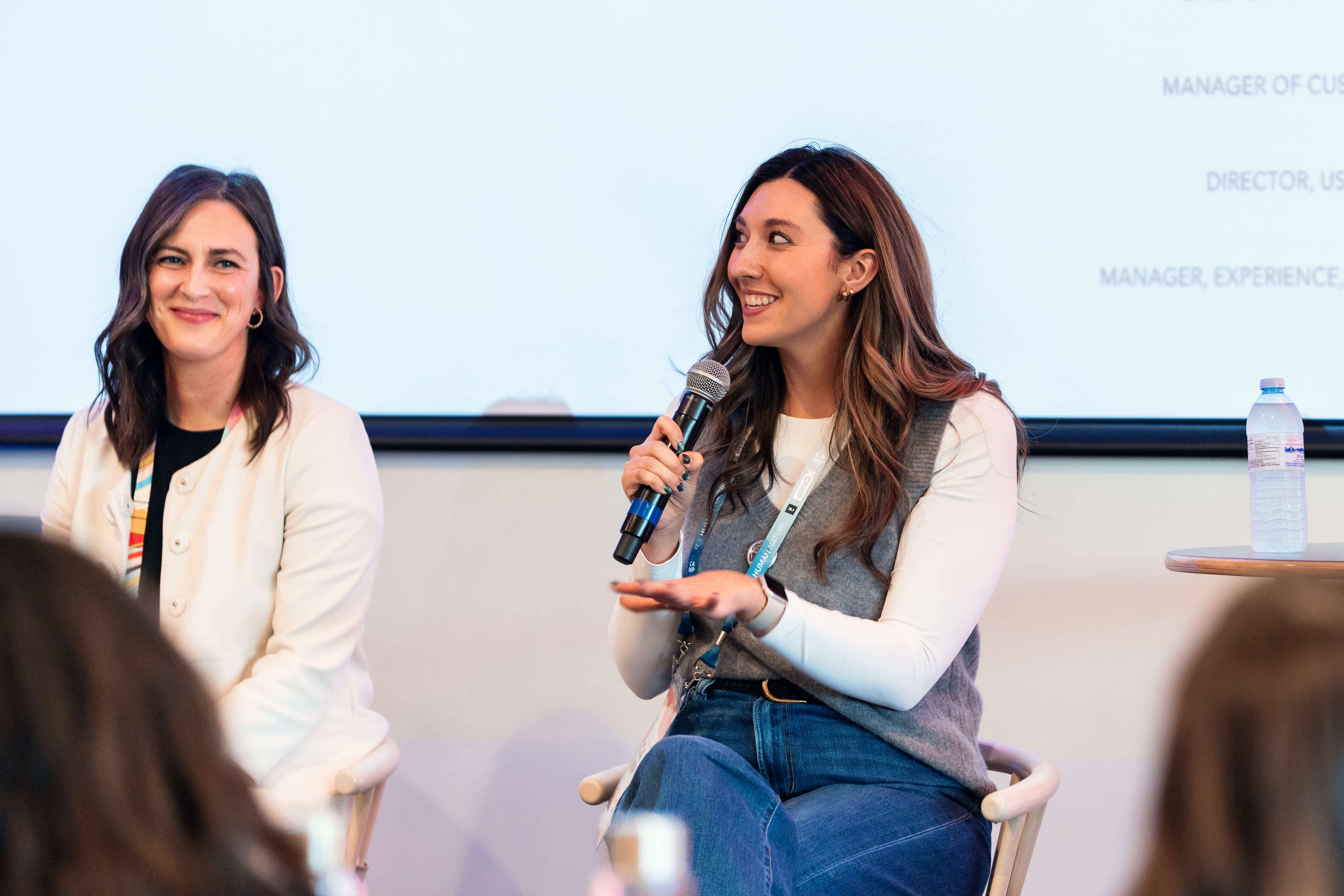 Two women seated on stage, one speaking into a microphone and smiling, during a panel discussion.