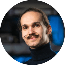 A man with a moustache wearing a turtle neck sweater, looking confidently at the camera.

