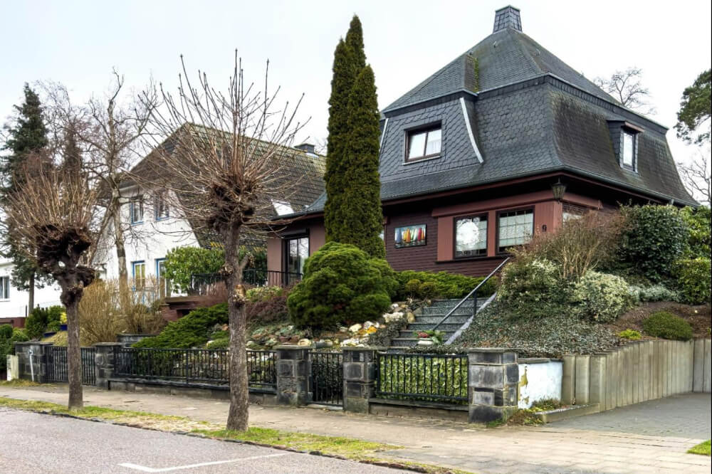 A house with a large roof surrounded by a wooden fence in a grassy area.

