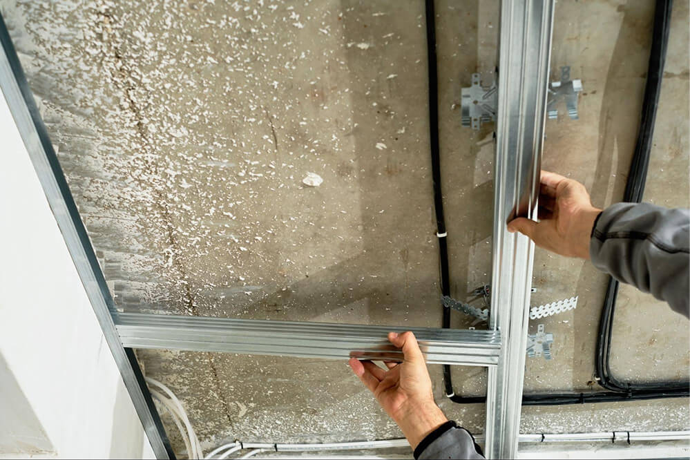 A man repairs a window frame inside a garage, surrounded by tools and materials.

