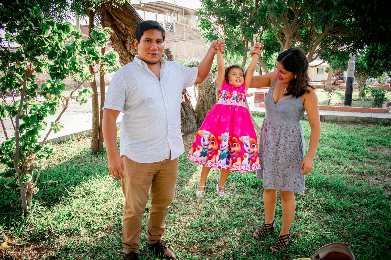 Parents and their young daughter playing together in a sunny garden.