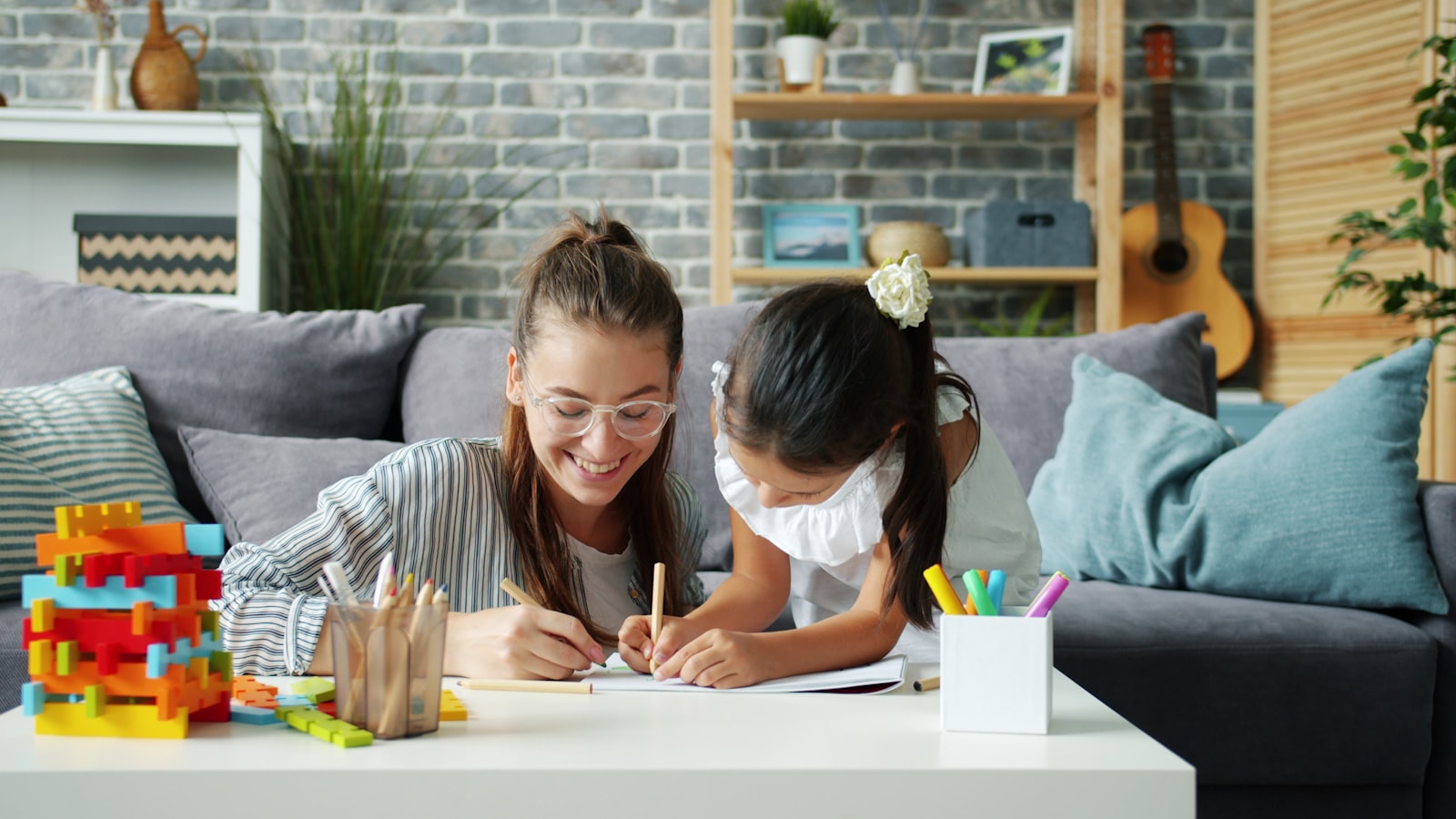 A parent and child drawing together at a table in a bright living room.