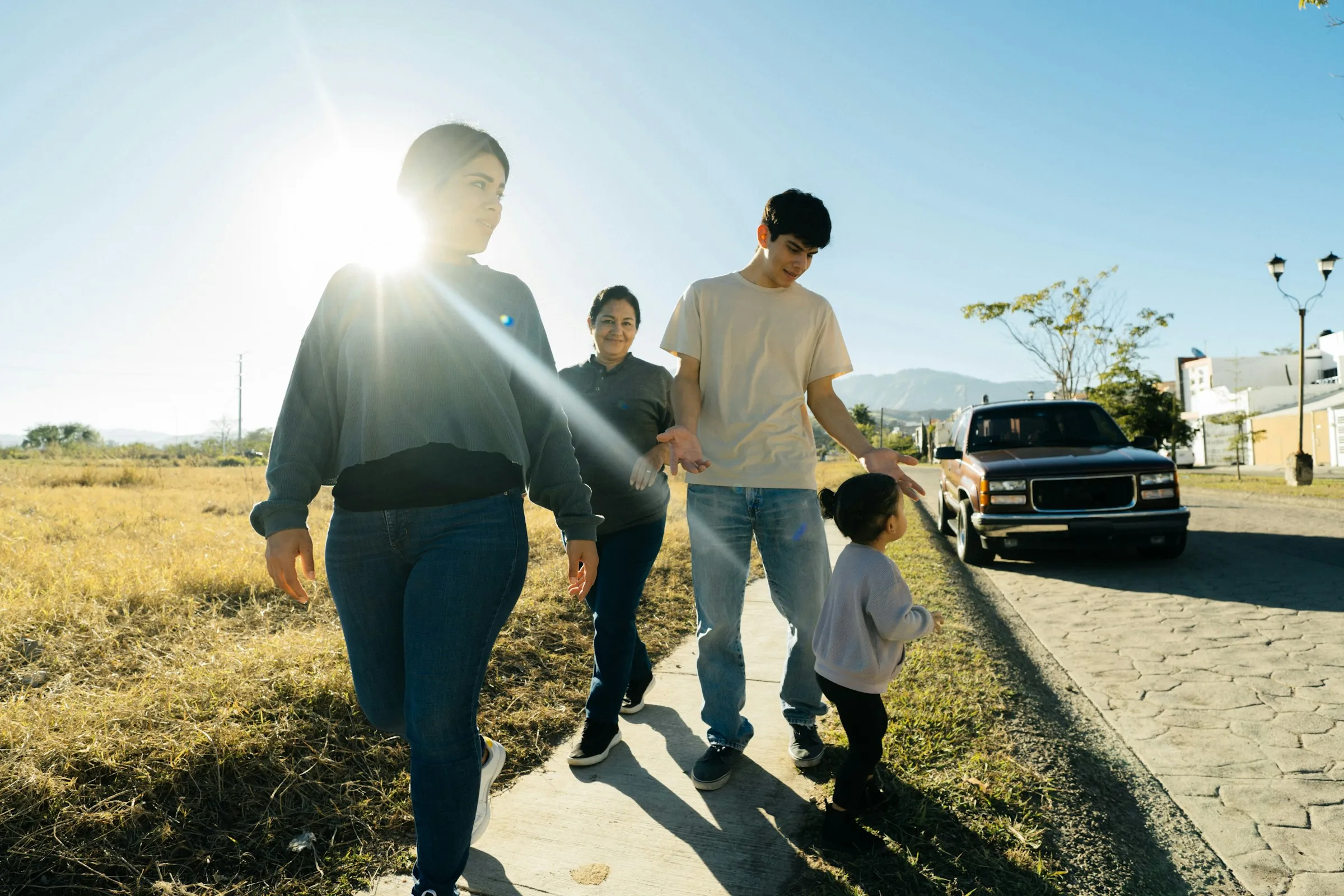 A family with teens walks along a sidewalk past golden hills.