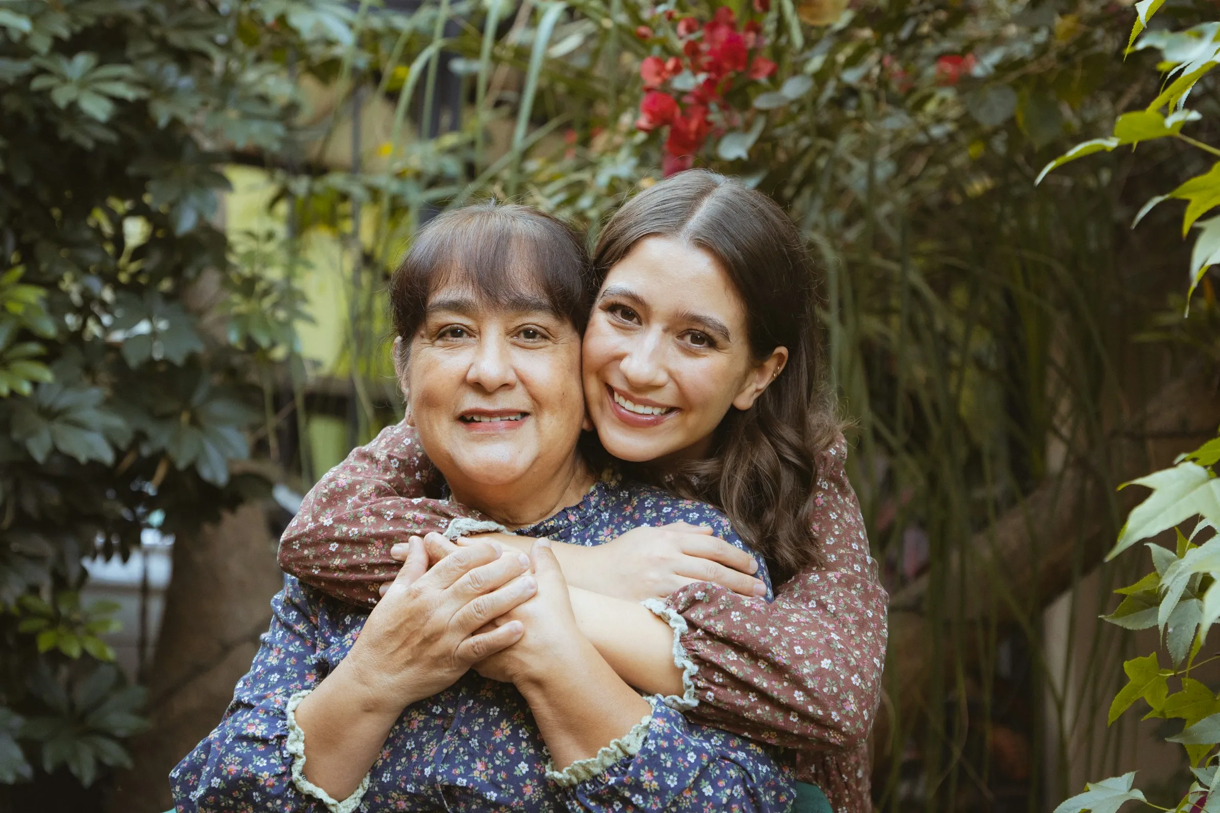 A young woman hugs an older woman in a garden.