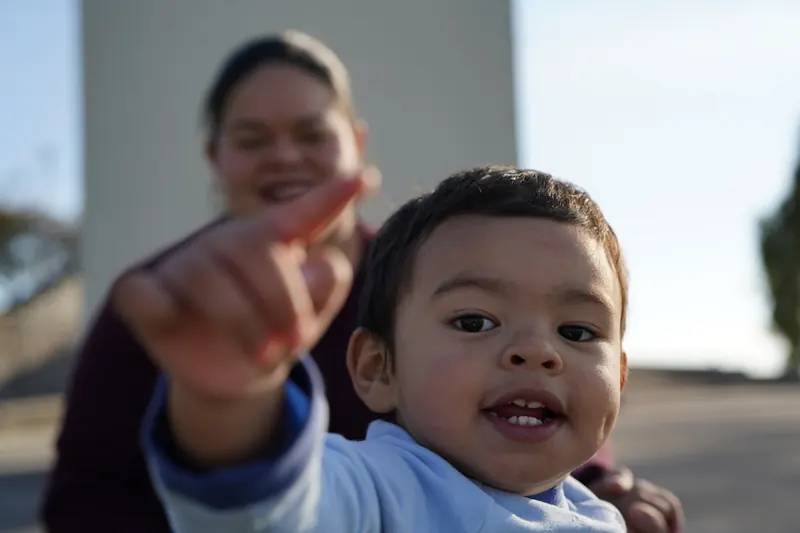 A young child pointing while a parent looks on, communicating with a gesture.