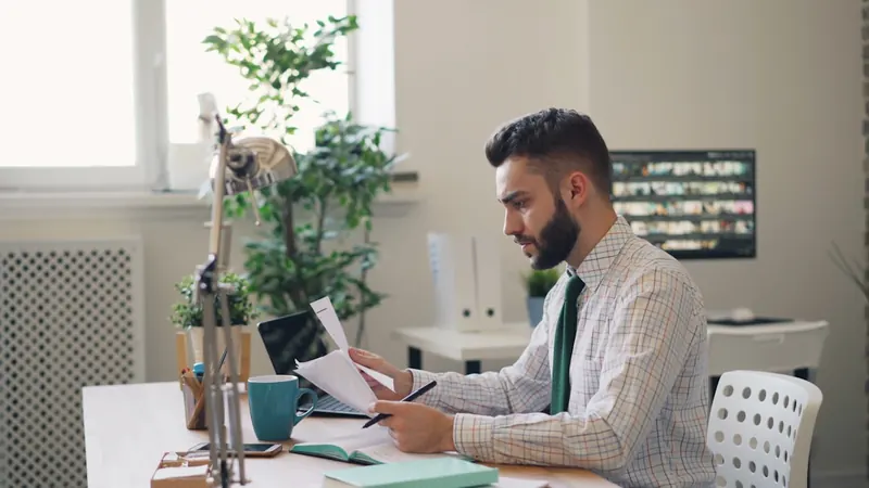 A person reviewing paperwork at a desk in a bright office.