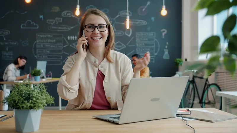 A parent on a phone call with a laptop and notebook at home.