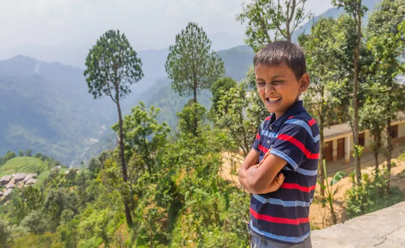 A confident young child standing outdoors on a bright day.