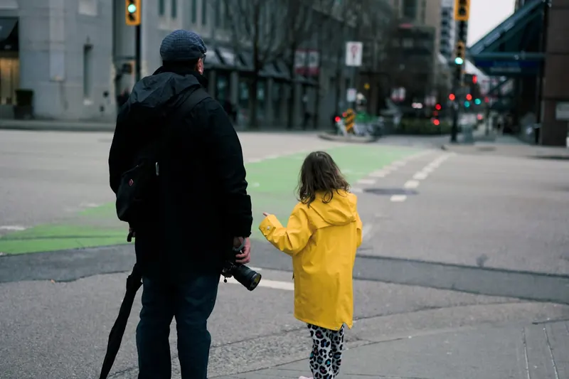A parent and child holding hands as they cross a city street together.