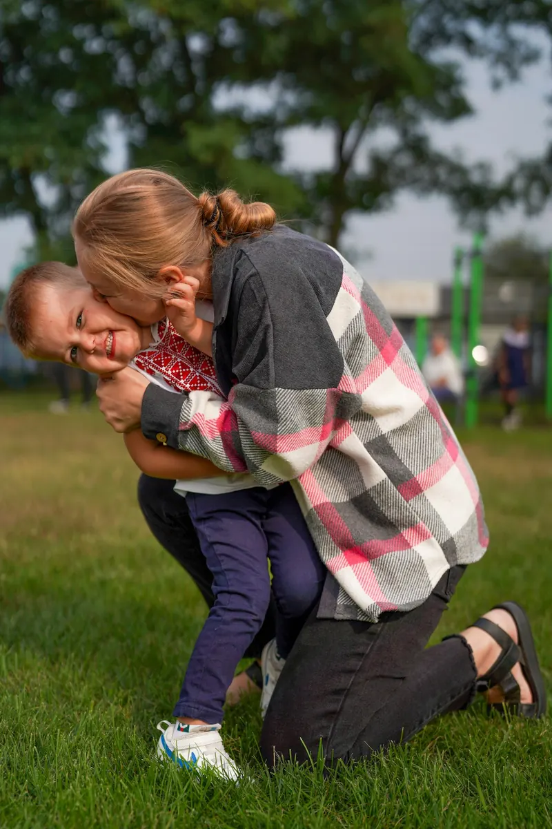 An adult kneeling to embrace a child at their eye level outdoors.