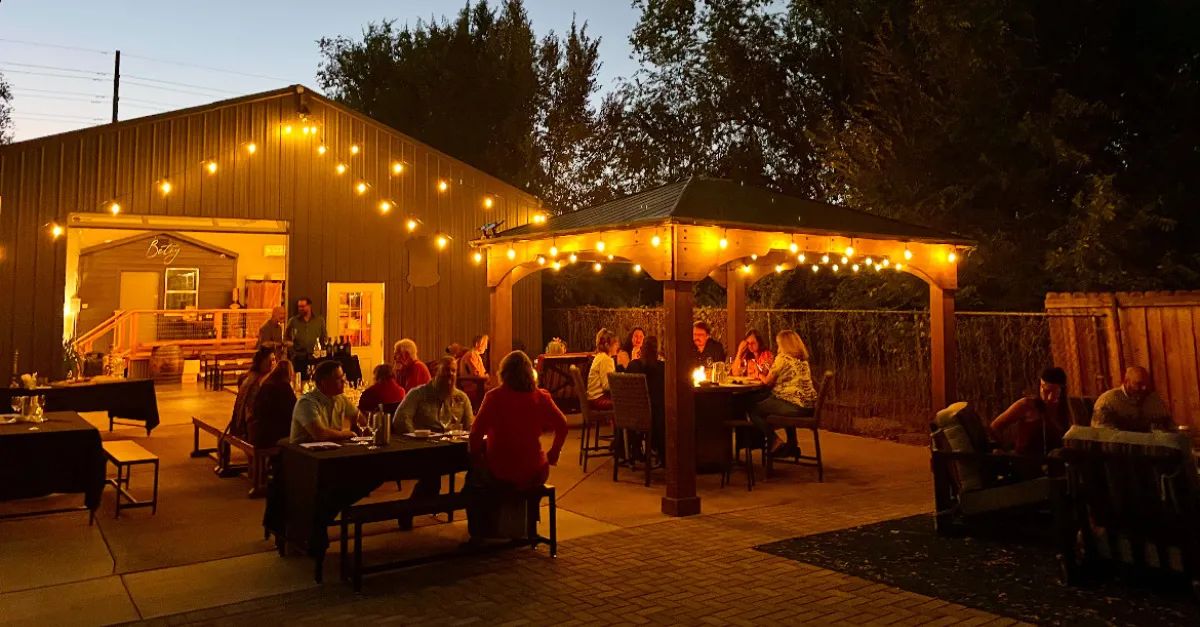 The Starlight Patio event space at The Betsy at night with the string lights on and firepits going. People are gathered all around enjoying wine. 