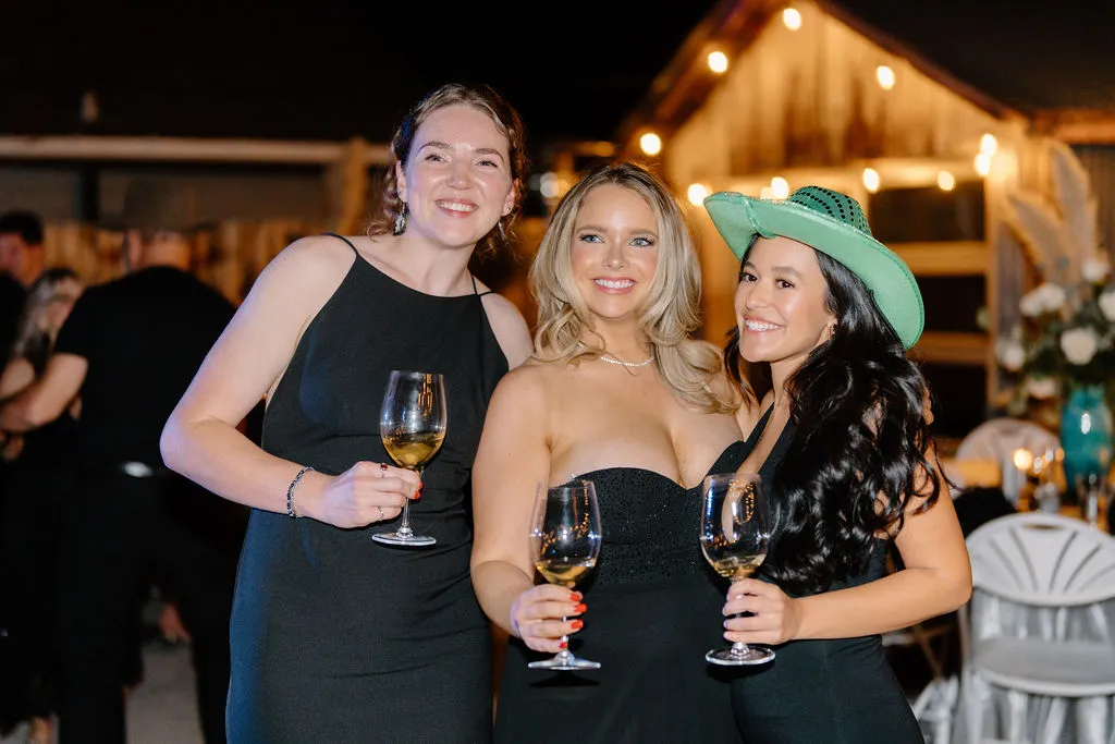 A group of three wedding guests on The Starlight Patio during the wedding reception having fun and drinking wine.