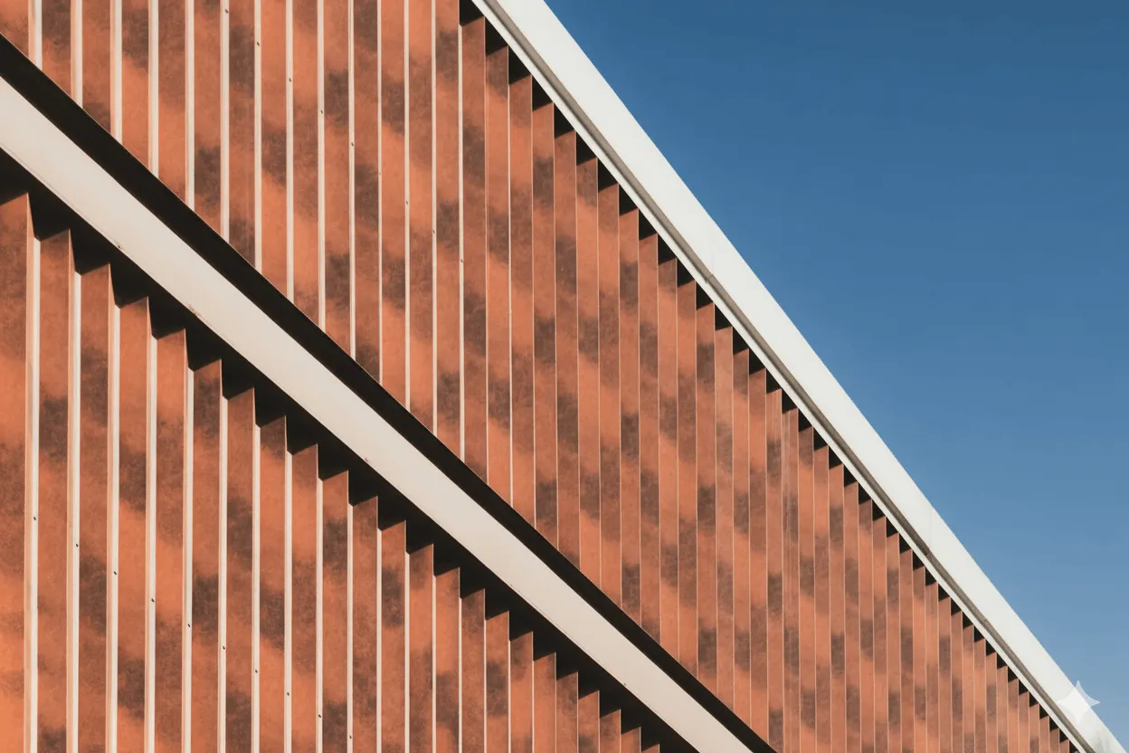 Close-up of a modern architectural facade with vertical orange panels and white diagonal lines against a clear blue sky.
