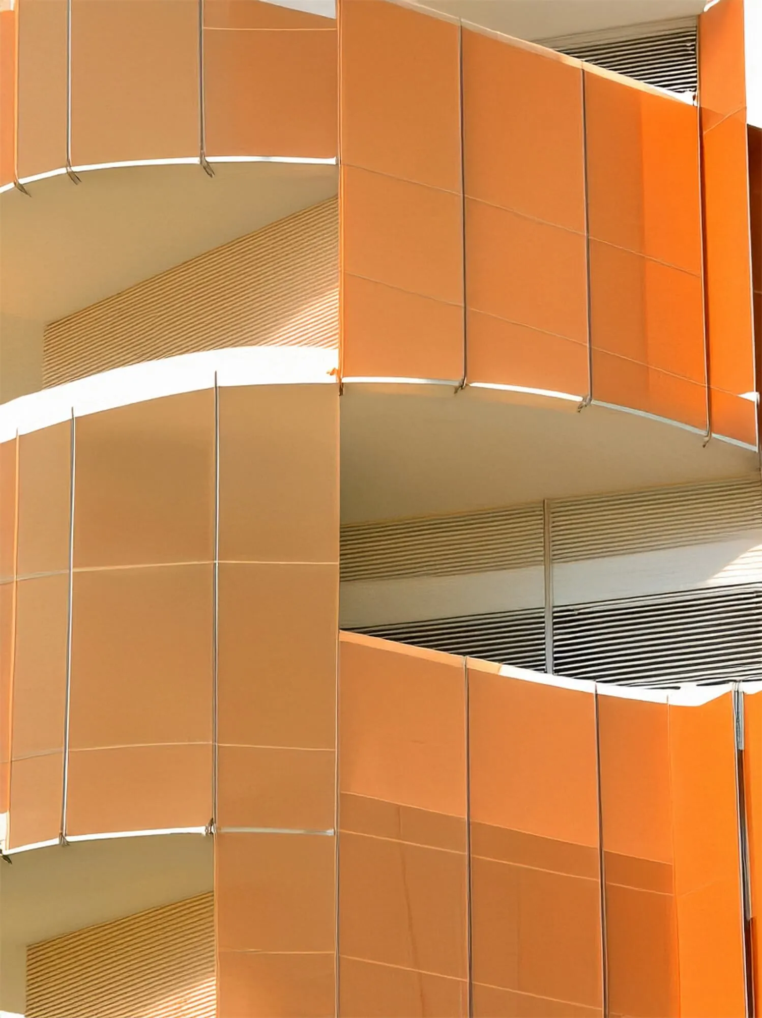 Modern building corner with an orange upper section featuring large windows against a blue sky with some tree branches.