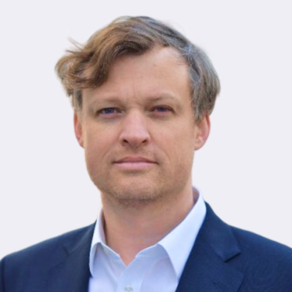 Porträt eines Mannes mit blonden Haaren und blauem Anzug vor hellem Hintergrund.