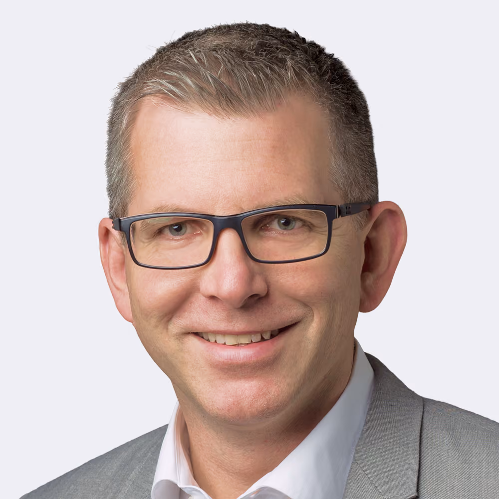 Älterer Mann mit weißem Hemd und Brille, hebt leicht die Faust vor sich.