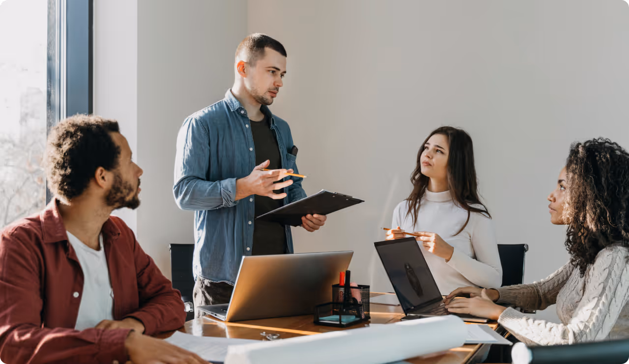 Quatre collègues en réunion dans une salle lumineuse, échangeant de la formation Outlook autour de leurs ordinateurs portables.