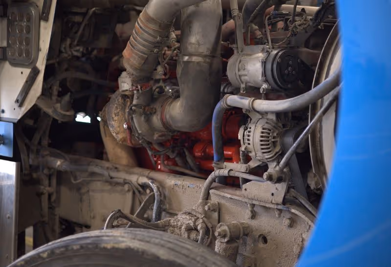 Close-up view of a diesel truck engine with alternator, hoses, and mechanical components exposed, showing detailed parts during maintenance inspection.