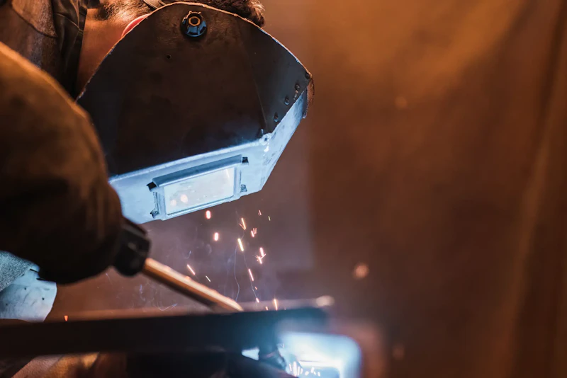 Trailer fabrication service showing technician welding heavy-duty metal component with sparks and protective welding shield.