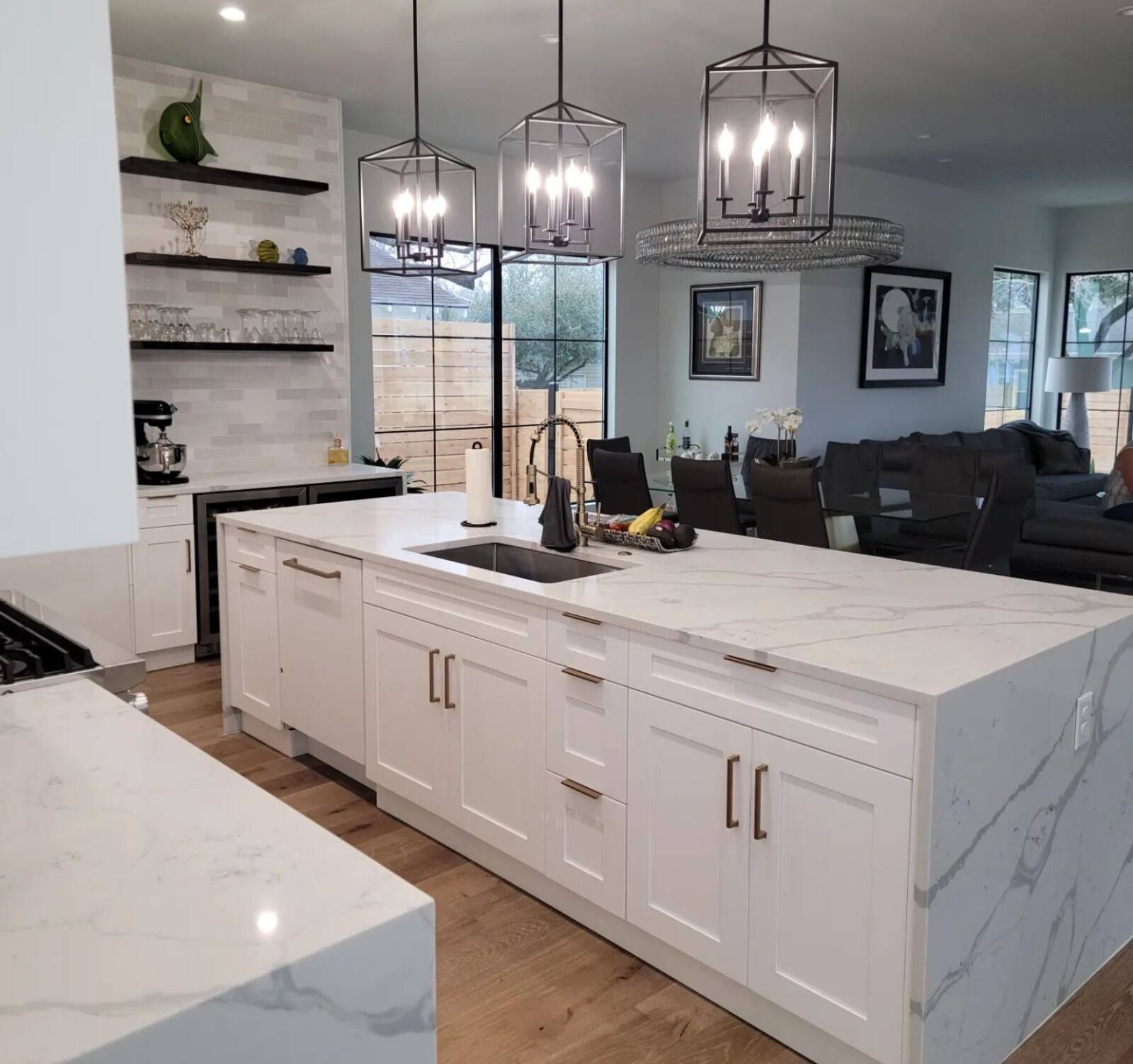 A bright, modern kitchen featuring a large white quartz island, and white shaker cabinets with gold hardware.