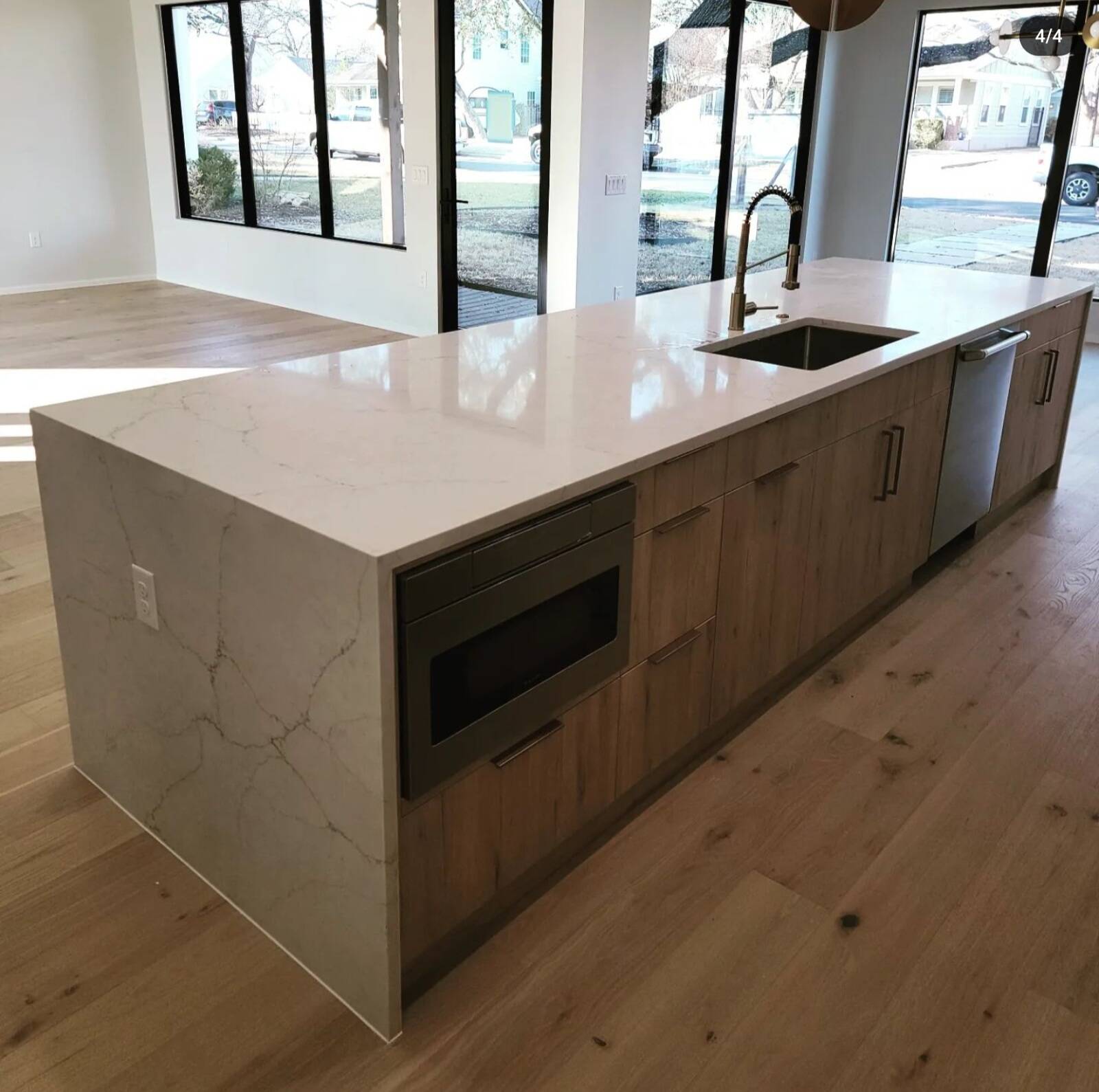 Long kitchen island with a white quartz waterfall edge and natural wood-grain cabinetry.