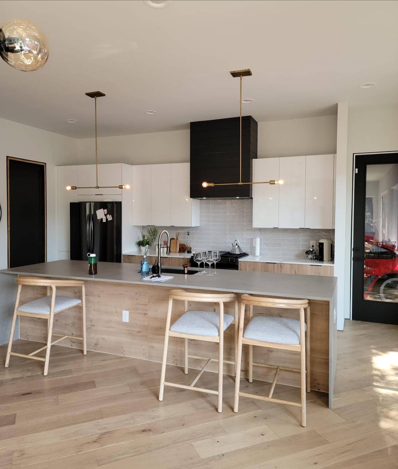 Kitchen with white flat-panel cabinets, a black chimney range hood, and a wood-paneled island with seating.