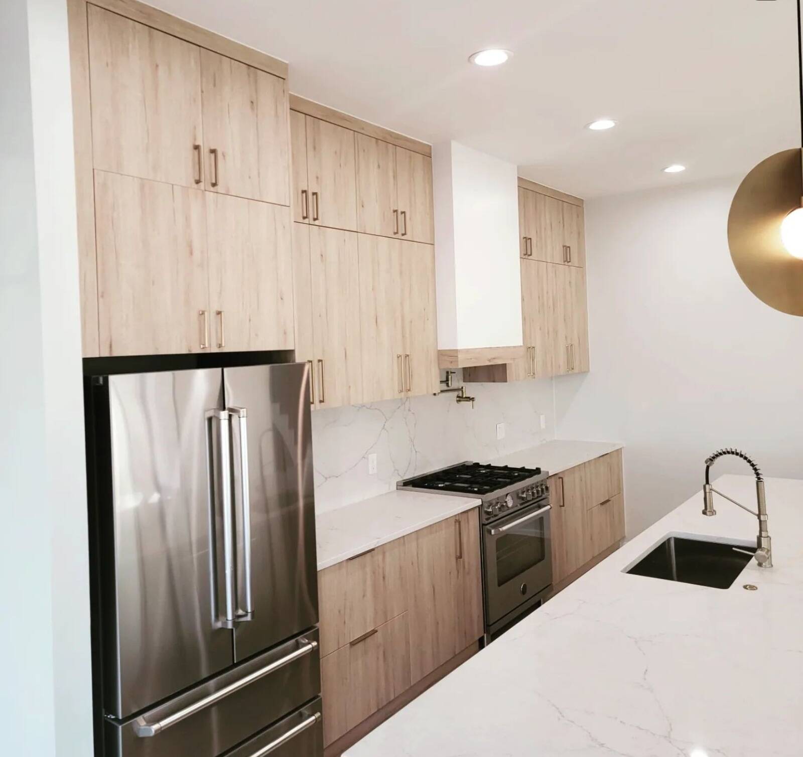 Contemporary kitchen featuring tall, light wood-grain flat-panel cabinets and a stainless steel refrigerator.