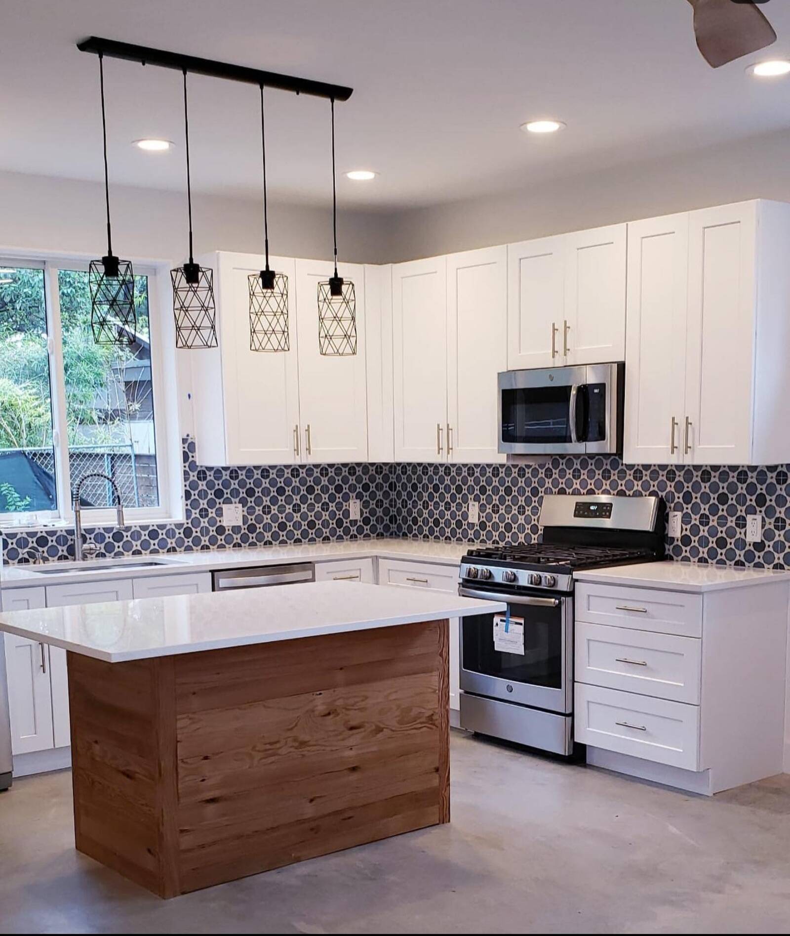 A bright kitchen with white shaker cabinets, a wood-paneled island, and a distinctive blue and white patterned tile backsplash.