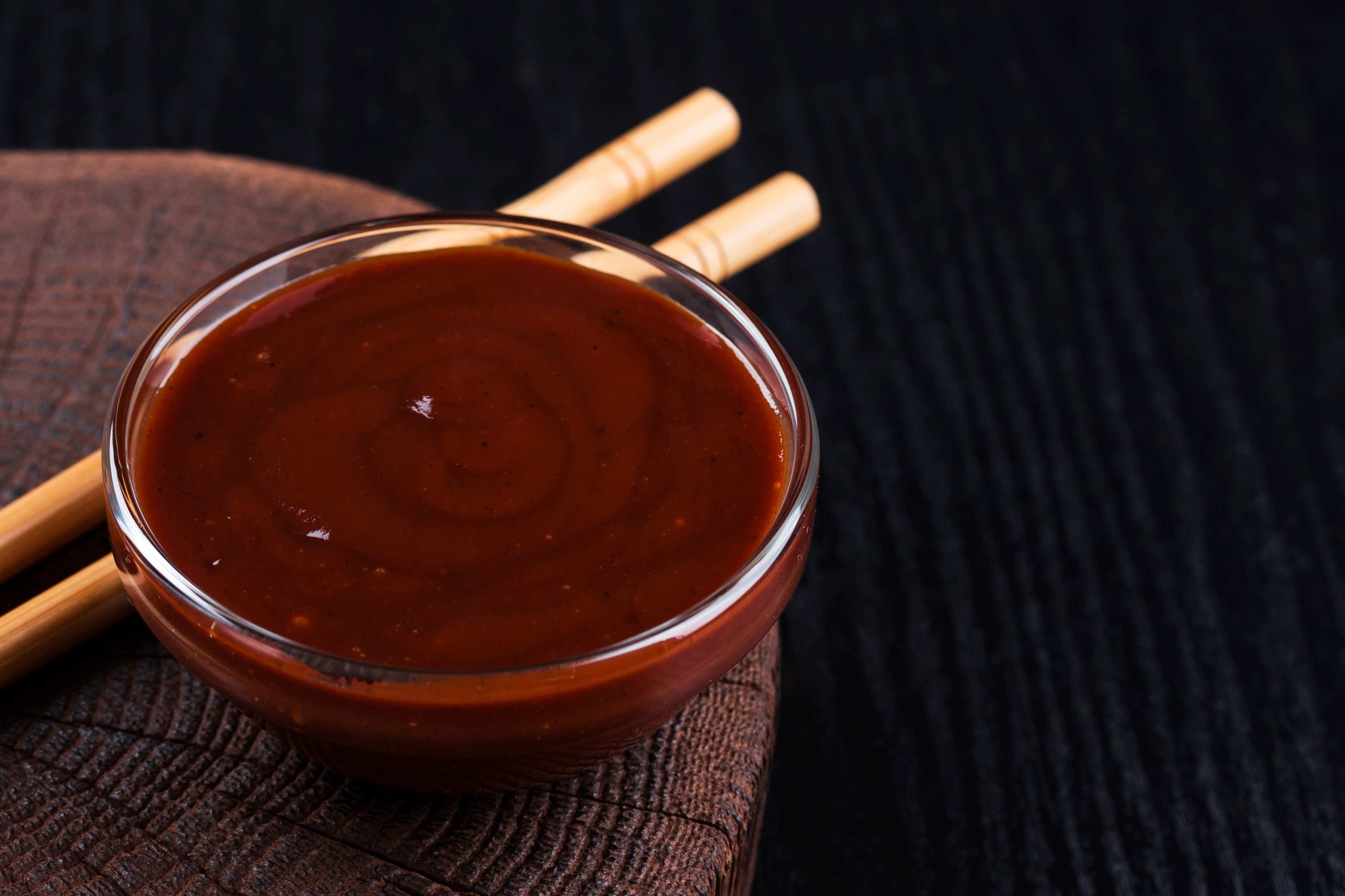 Korean BBQ sauce sits on a dark wooden board, with a pair of bamboo chopsticks resting beside it