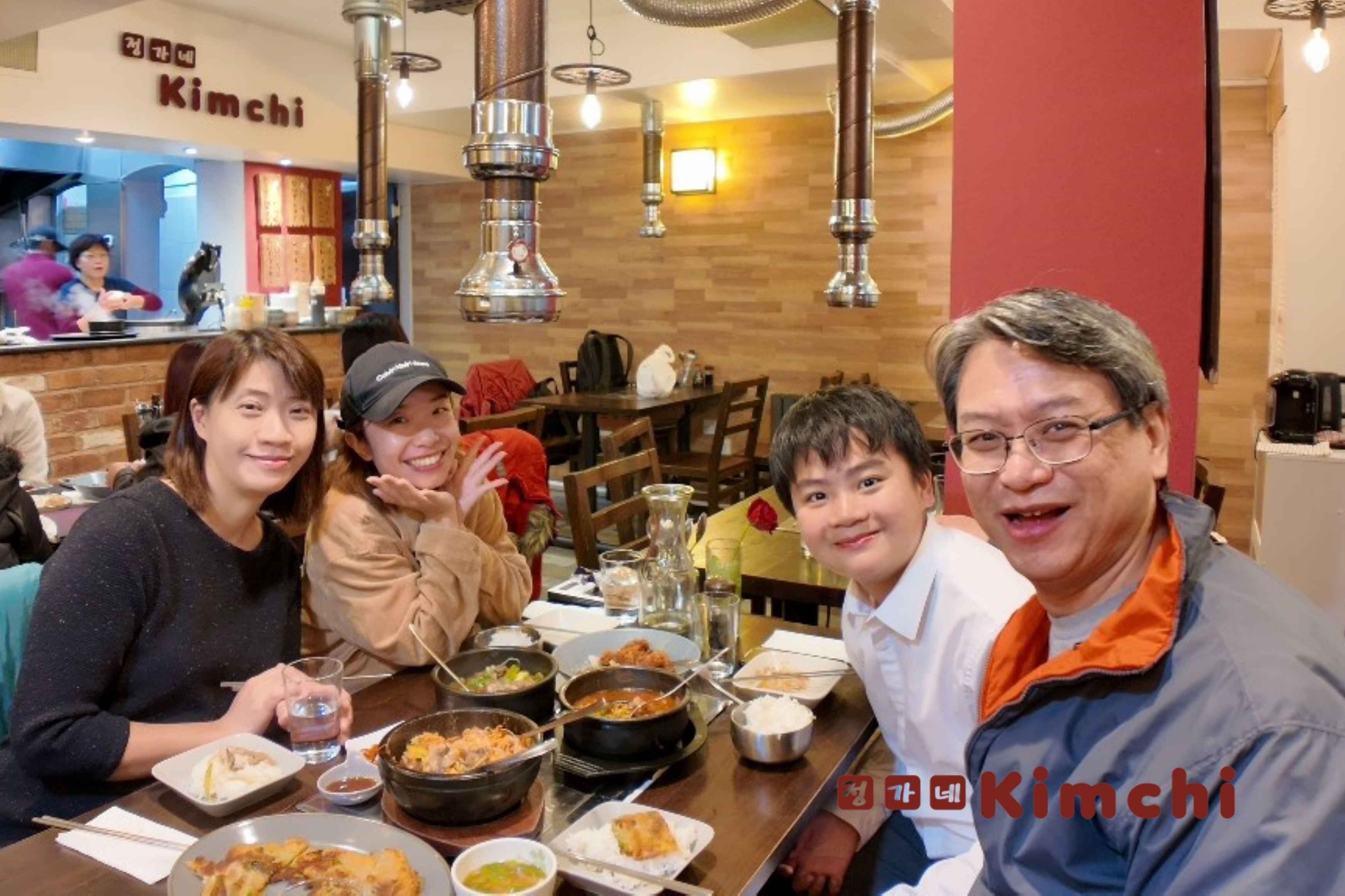 A smiling family enjoying a Korean BBQ meal together at Kimchi restaurant in Selly Oak, Birmingham, with sizzling dishes and side plates on the table.