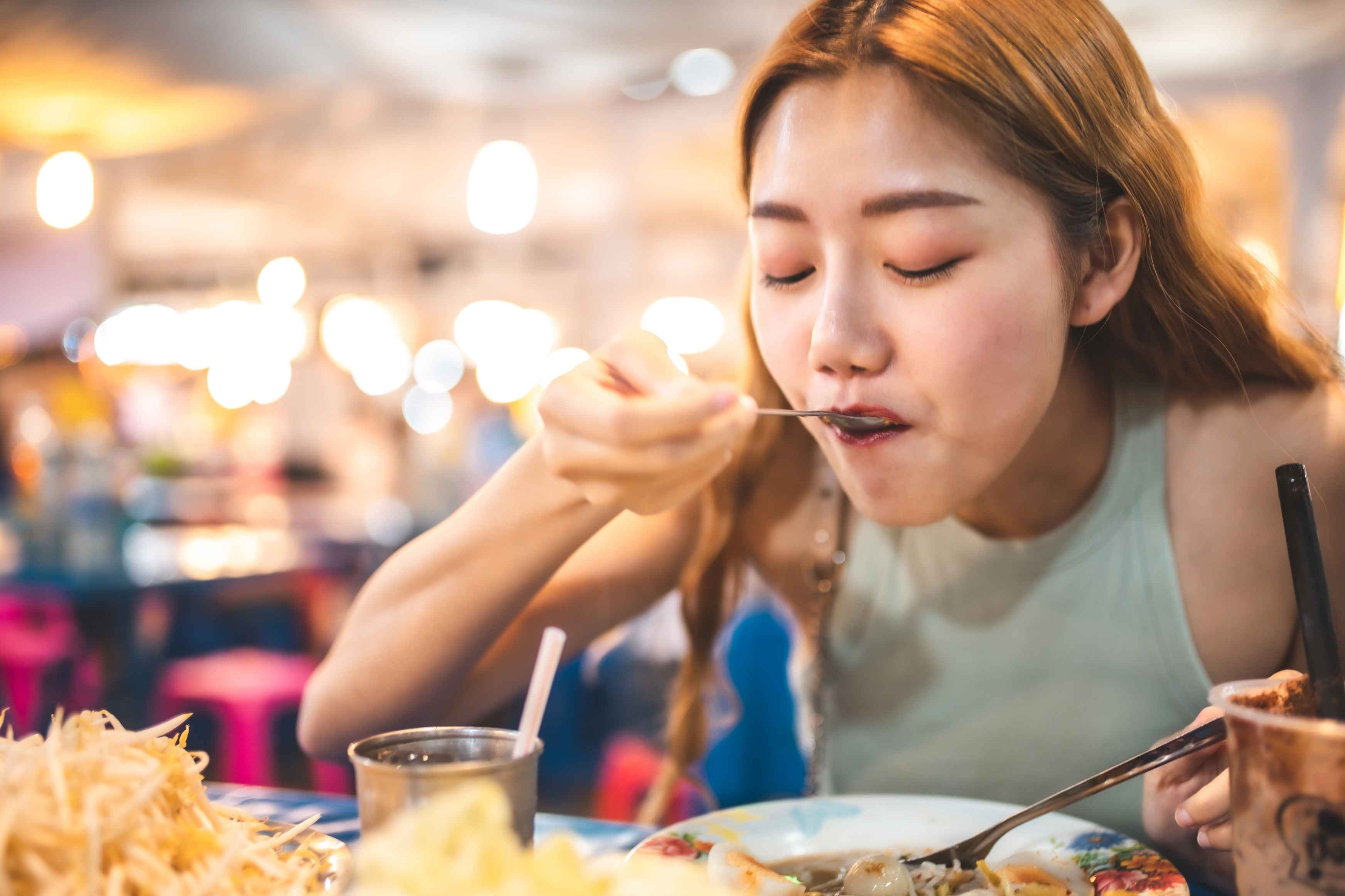 Woman sampling a spicy dish while dining at a Korean restaurant.