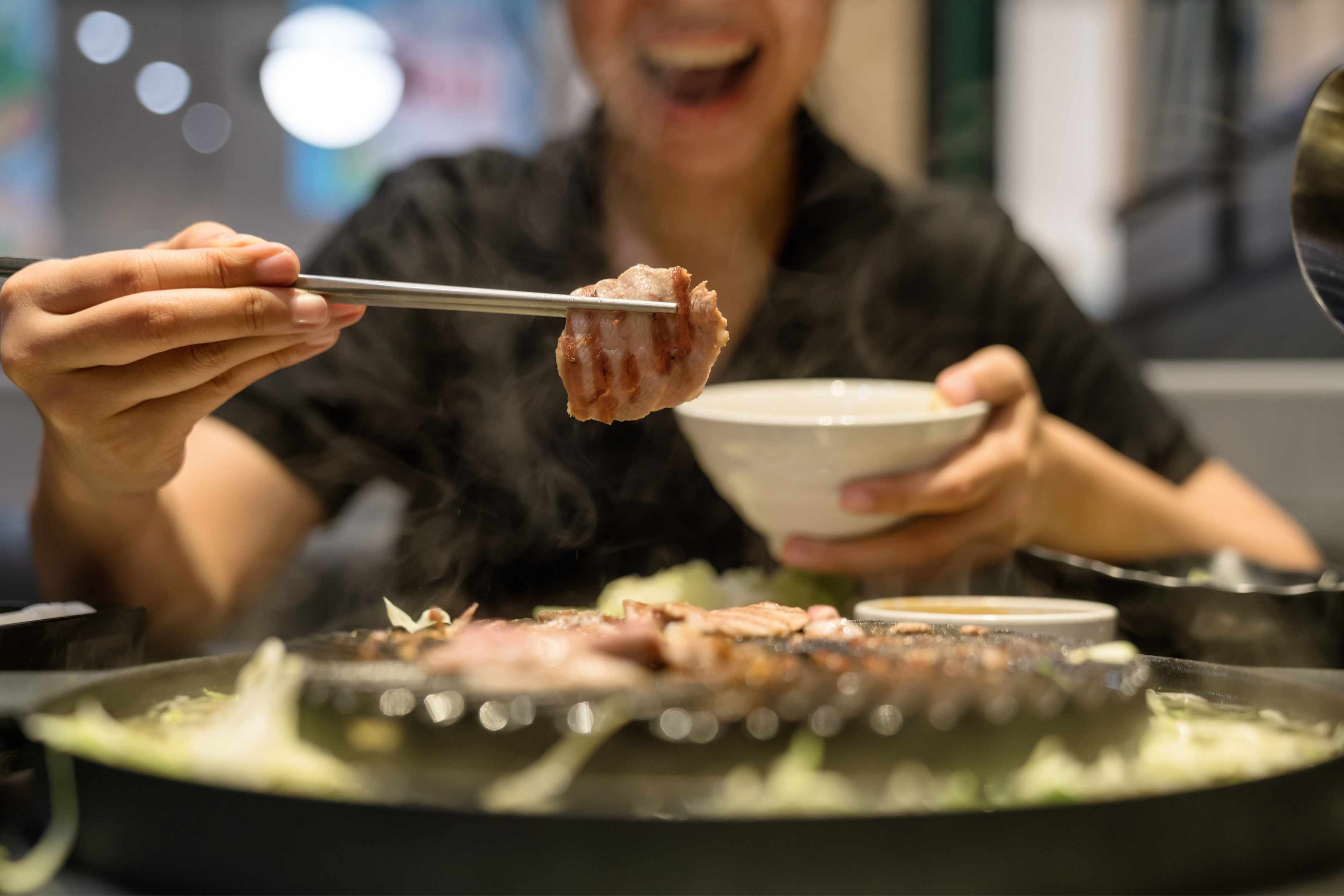 Freshly grilled Korean BBQ being picked up with chopsticks at the table