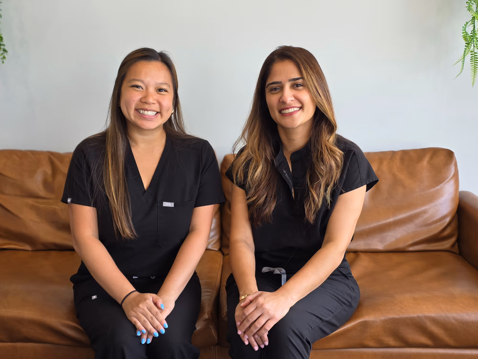 A couple of women sitting on top of a brown couch.