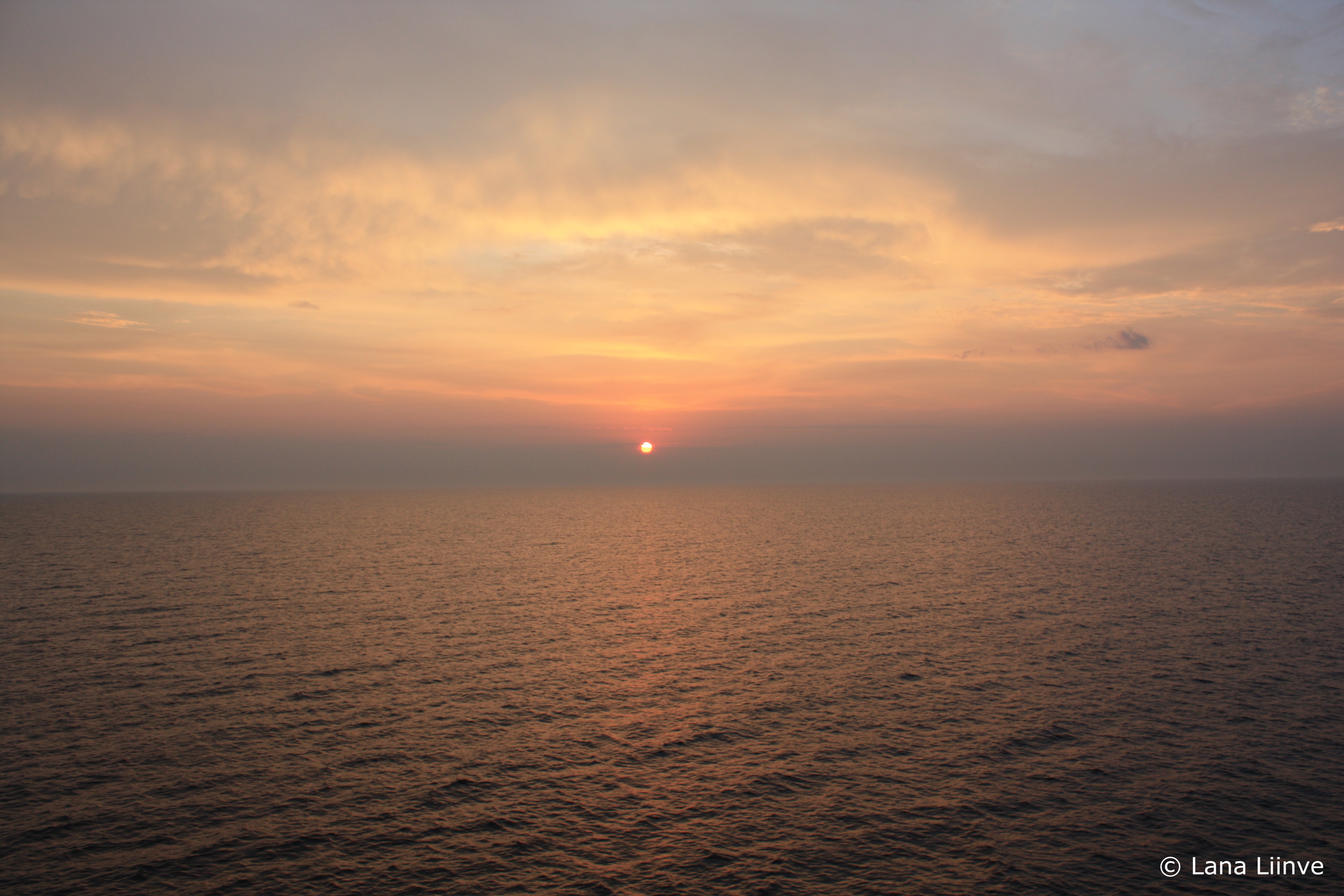 A photo of a hazy pink, orange, and purple hued sunset over an ocean