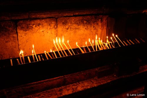 A photo of numerous thin, lit prayer candles inside the Church of the Holy Sepulchre in Jerusalem